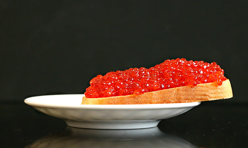 Slice of bread topped with red salmon caviar on a white plate