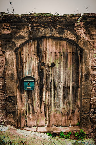 Weathered wooden gate with blue mailbox in stone archway