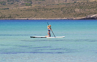 Woman paddleboarding on turquoise sea with coastal hills