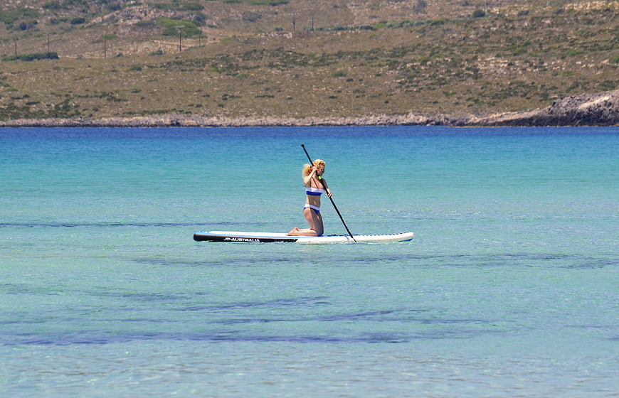 Woman paddleboarding on turquoise sea with coastal hills