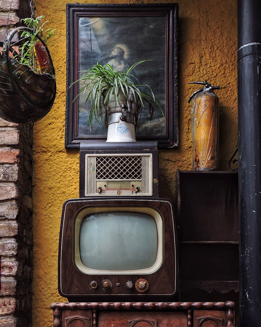 Vintage Television and Radio Stacked Against Yellow Wall
