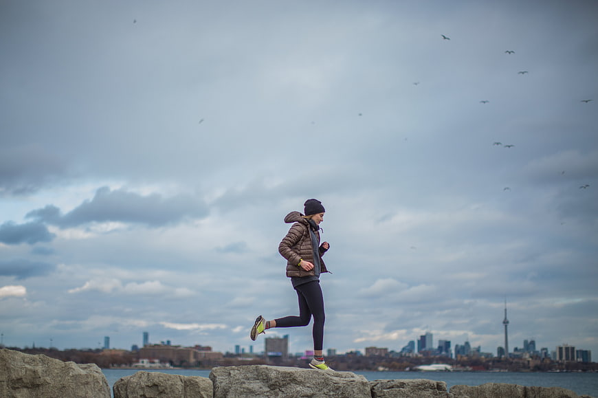 Woman Running on Rocks with City Skyline Background