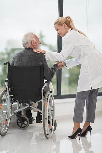 Female doctor comforting elderly man in wheelchair