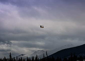 Helicopter Flying Over Snowy Mountain Peaks Under Cloudy Sky
