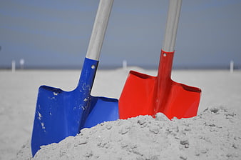 Red and Blue Shovels Stuck in Sand on Beach