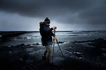 Photographer with tripod on dark volcanic beach under stormy sky