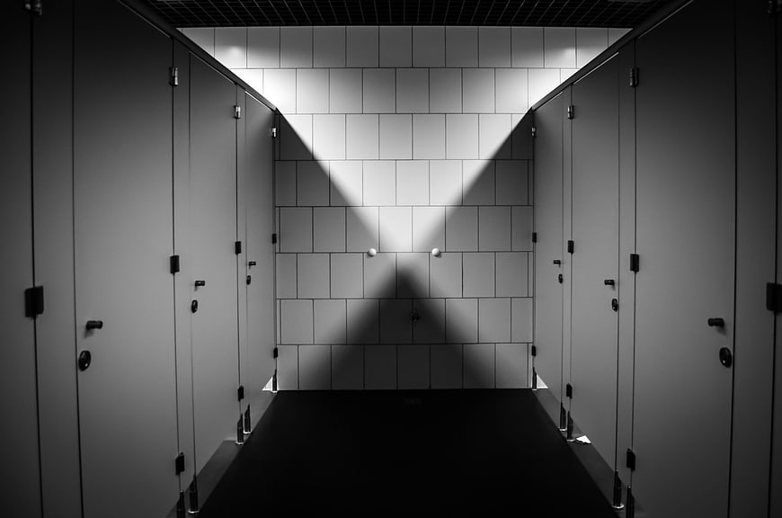 Symmetrical black and white public restroom stalls with dramatic lighting