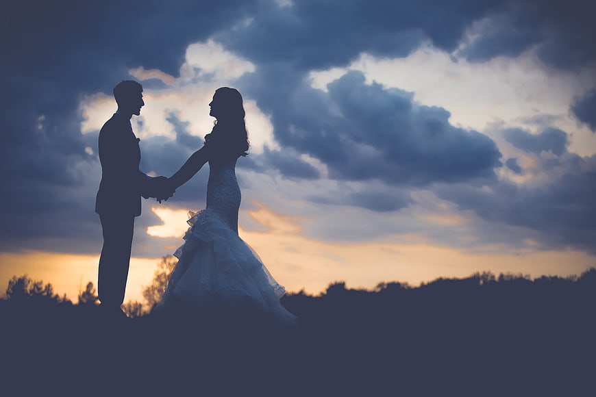 Silhouette of wedding couple holding hands against dramatic sunset sky
