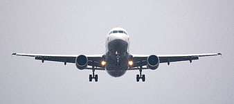 Front view of white commercial airplane landing with landing gear down