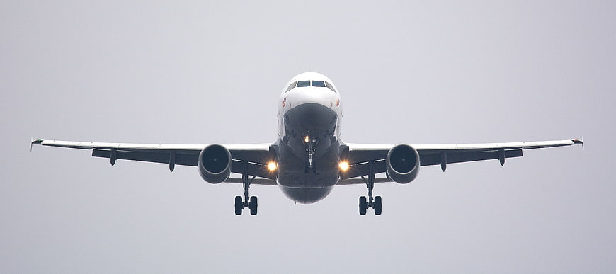 Front view of white commercial airplane landing with landing gear down