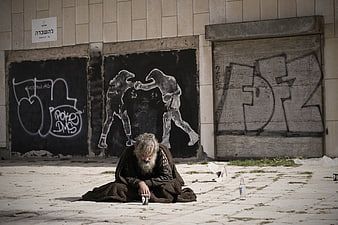 Homeless man sitting on pavement in front of urban graffiti wall