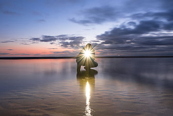 Silhouette of person holding sun on beach at sunset