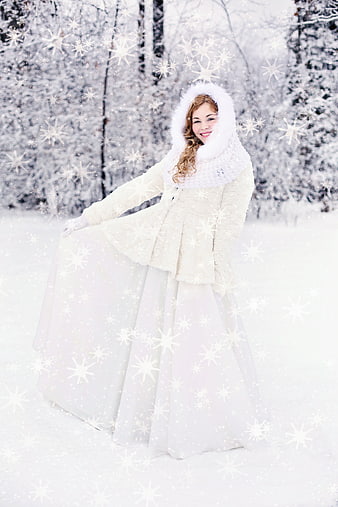 Young woman in white winter coat and long dress in snowy forest
