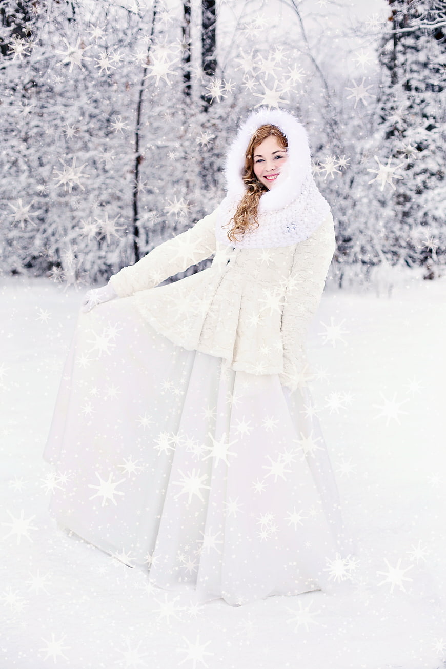 Young woman in white winter coat and long dress in snowy forest