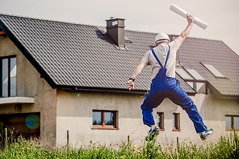 Builder jumping with blueprints in front of new house