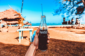Hand Holding Coca-Cola Bottle at Tropical Beach
