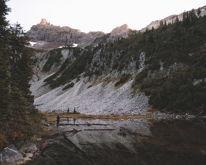 Lone Hiker Standing by Mountain Lake with Forest Reflections