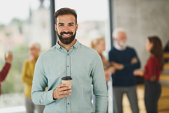 Smiling Bearded Man Holding Coffee in Modern Office