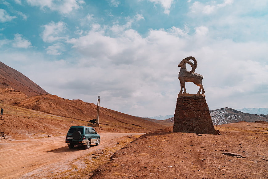 Green SUV driving past ram statue in desert landscape