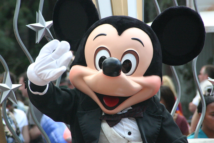 Mickey Mouse waving in a tuxedo at a parade
