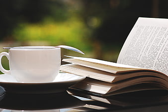 White Coffee Cup and Open Book on Glass Table Outdoors