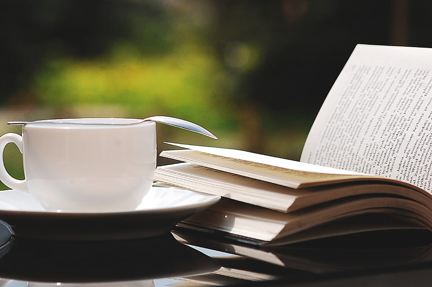 White Coffee Cup and Open Book on Glass Table Outdoors