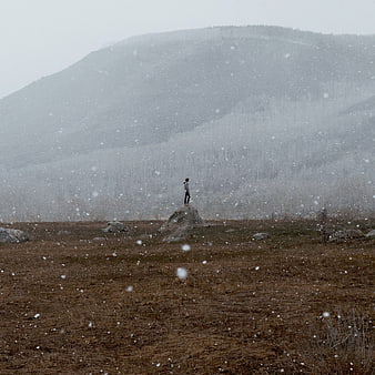 Lone figure standing on rock in snowy mountain landscape