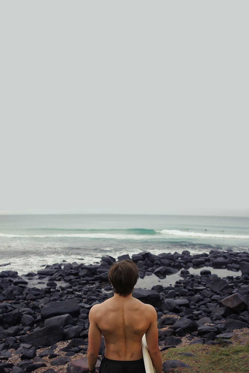 Surfer with surfboard looking out at ocean waves from rocky shore