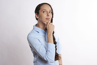 Thoughtful woman in blue shirt pondering with hand on chin