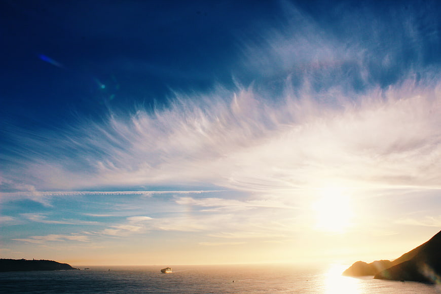 Dramatic Sunset Over Ocean with Streaked Clouds and Distant Boat