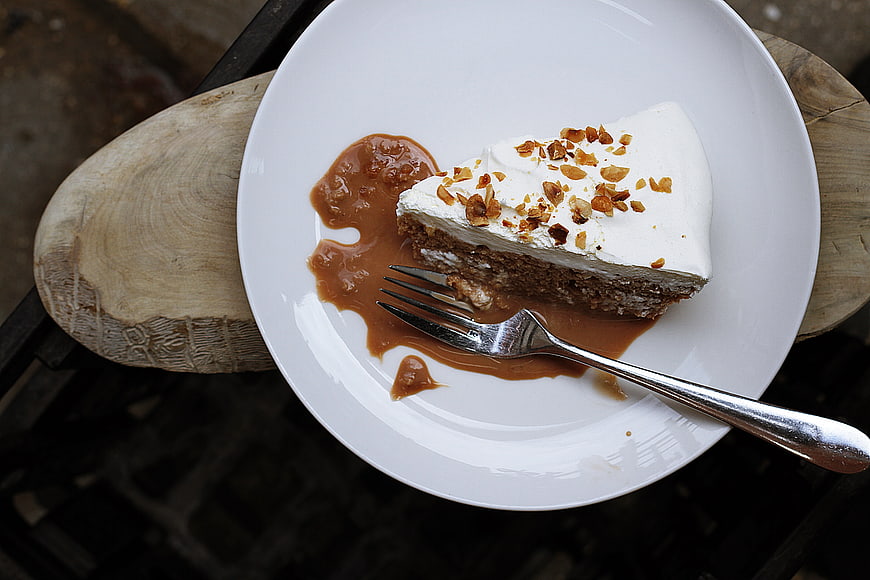 Slice of chocolate cake with caramel sauce and nuts on white plate