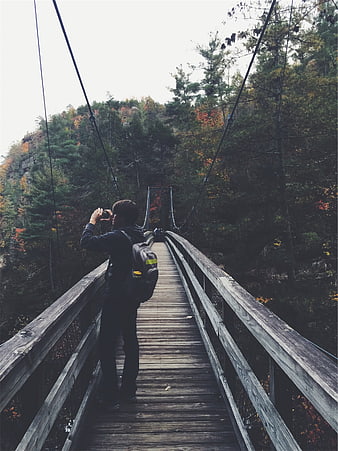 Hiker taking photo on wooden suspension bridge in autumn forest