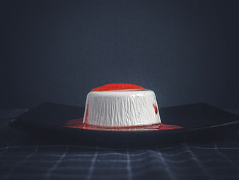 Dark moody panna cotta dessert with strawberry sauce on black plate