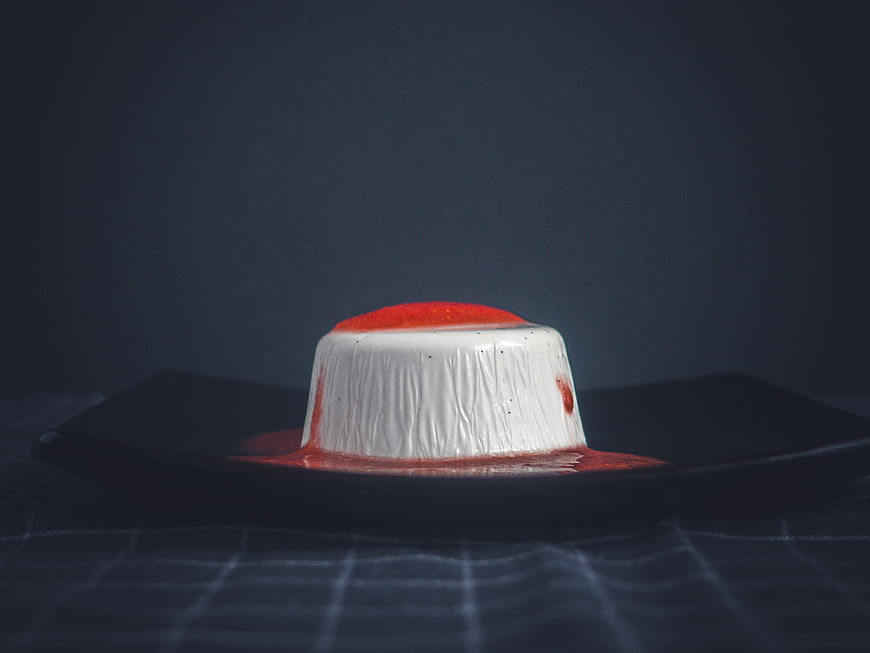 Dark moody panna cotta dessert with strawberry sauce on black plate