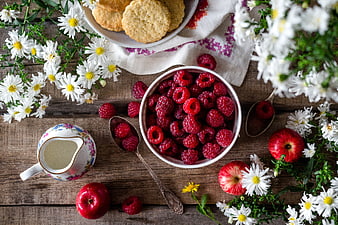 Flat lay of fresh raspberries, apples, and daisies on rustic wood