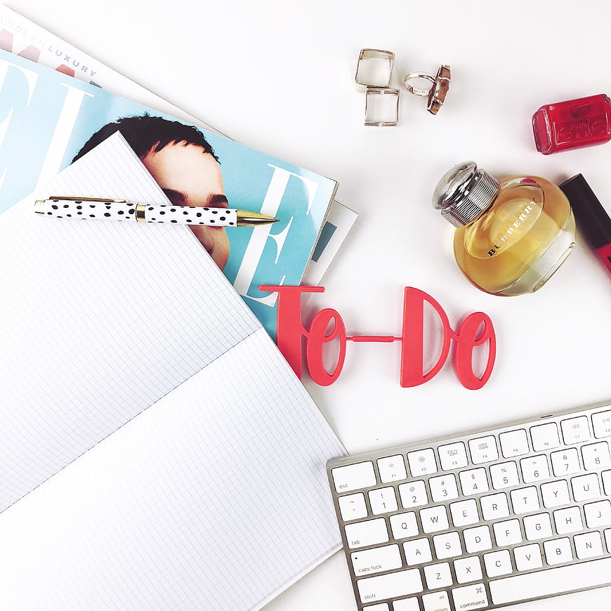 Flat lay of workspace with notebook, perfume, and to-do sign