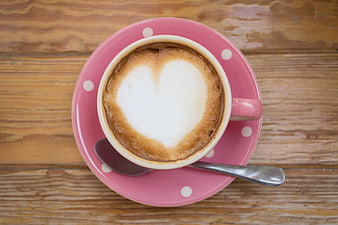 Heart-shaped latte art in pink cup on rustic wooden table