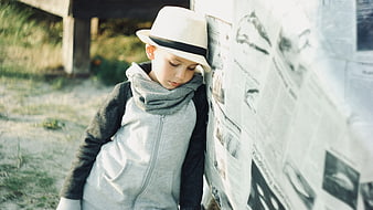 Pensive young boy in hat leaning against newspaper wall