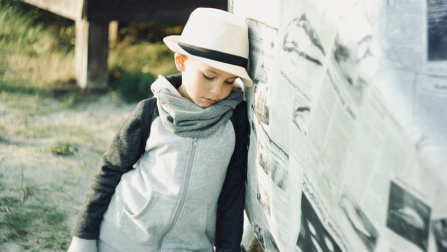 Pensive young boy in hat leaning against newspaper wall