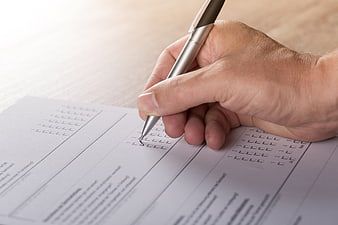 Hand filling out survey form with pen
