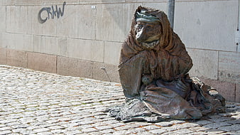 Bronze statue of a hooded figure on cobblestone street