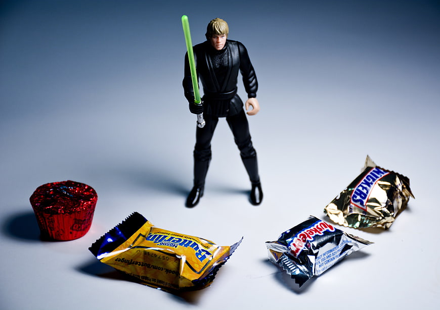 Star Wars action figure holding green lightsaber surrounded by candy wrappers