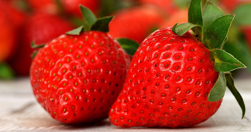 Close-up of two ripe red strawberries with green leaves on a white surface