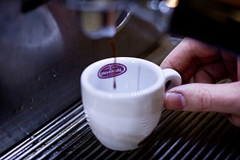 Barista pouring espresso into white cup from machine