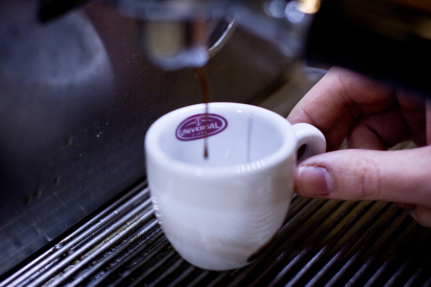 Barista pouring espresso into white cup from machine