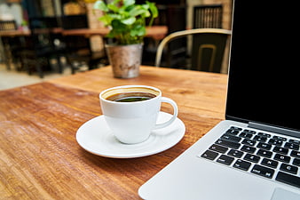 White coffee cup and laptop on wooden table in cafe