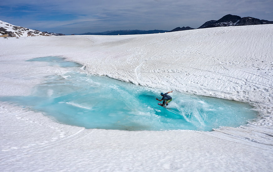 Snowboarder riding turquoise glacial stream in winter landscape