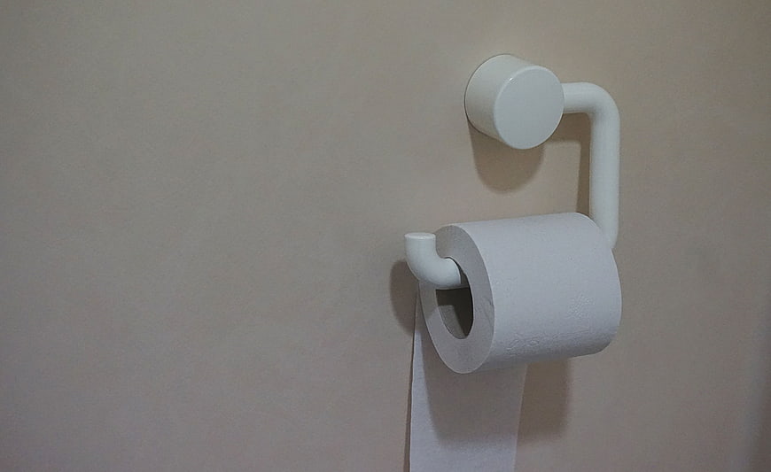 White Toilet Paper Roll on Holder Against Beige Wall