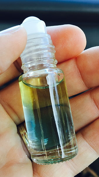 Hand holding small glass roller bottle with yellow essential oil