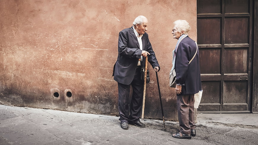 Two elderly people talking on a street corner